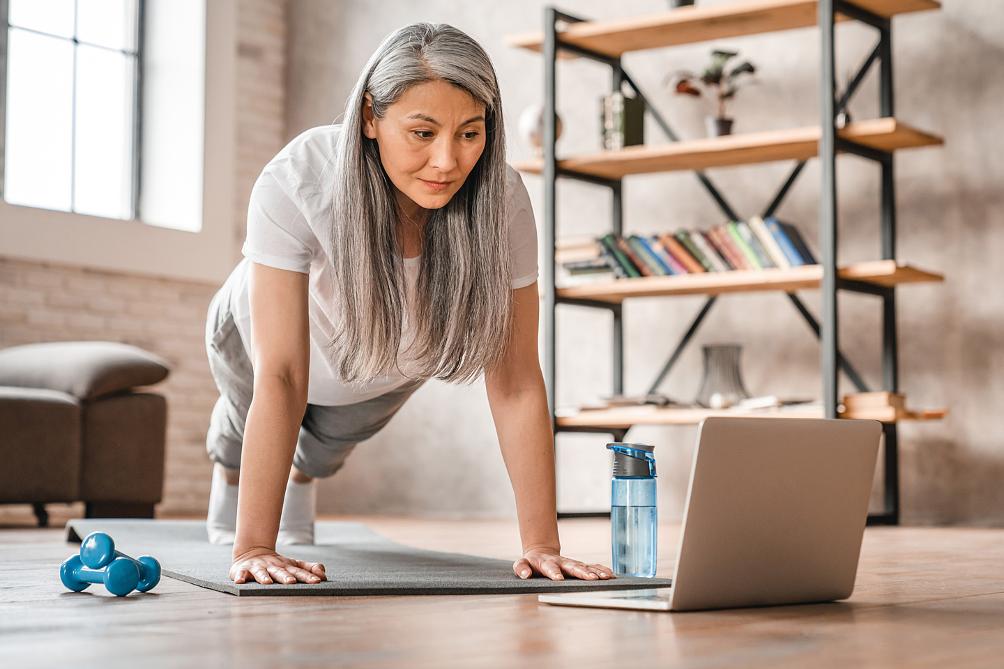 Frau mittleren Alters ist Fitness-Anfängerin und macht ein Workout im Wohnzimmer.
