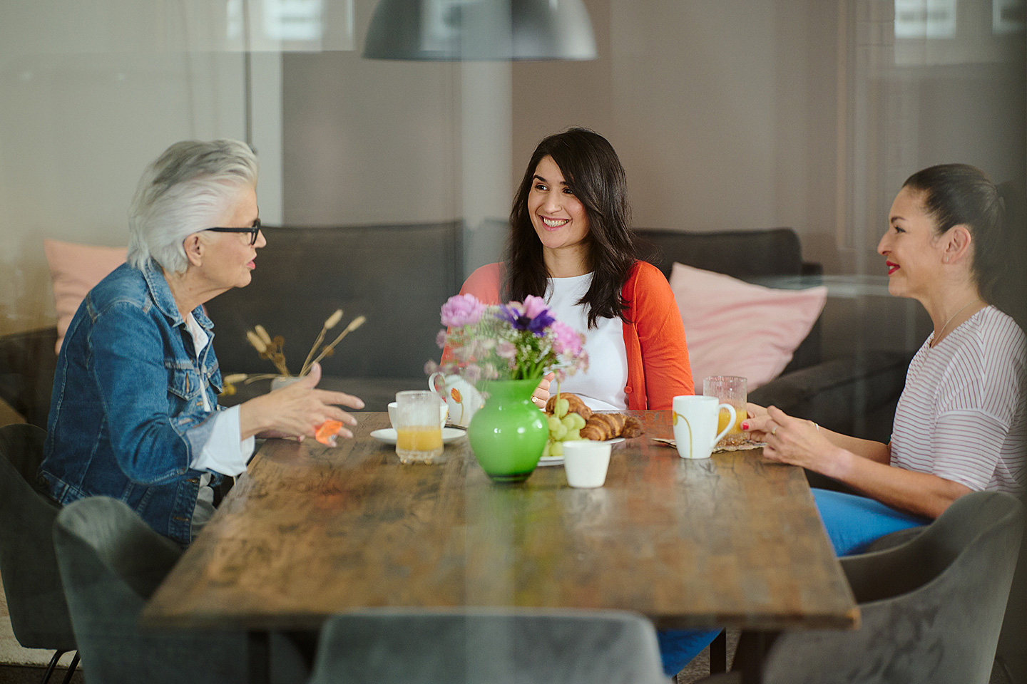 Drei Frauen unterschiedlichen Alters sitzen an einem Tisch mit Frühstück und sprechen über das Älterwerden.