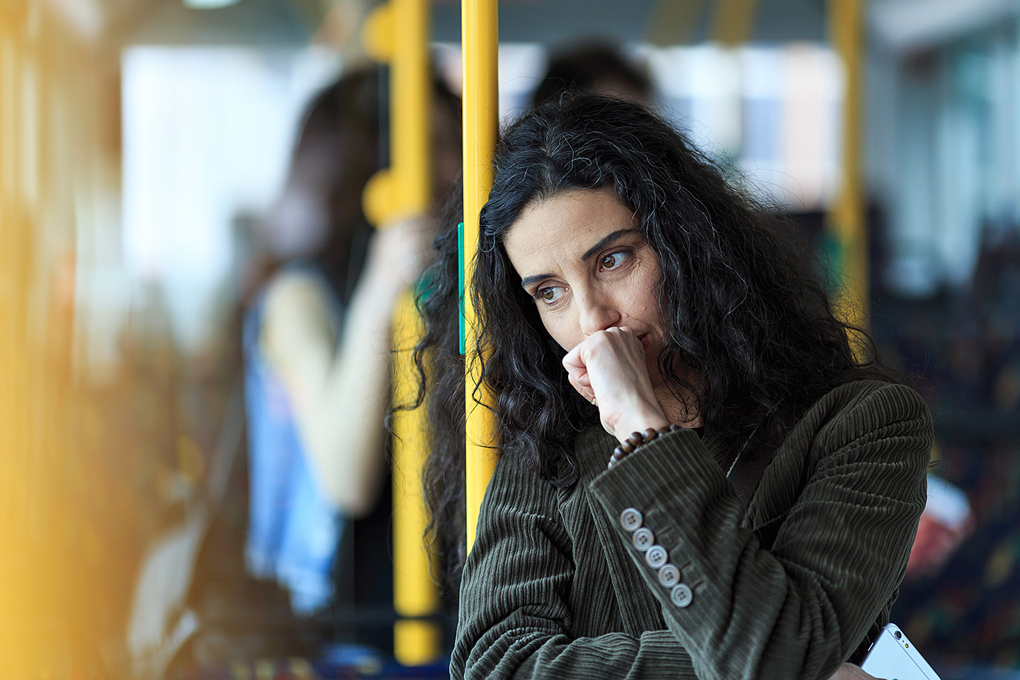 Eine junge Frau steht in einem Bus. Sie lehnt sich an eine gelbe Haltestange, dabei scheint sie intensiv zu grübeln.
