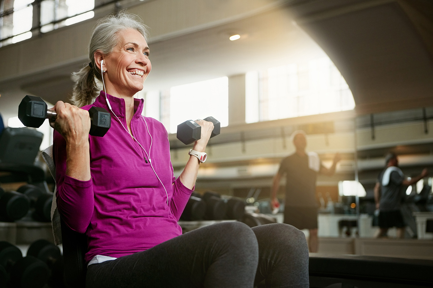 Eine ältere Frau im Fitnessstudio führt mit Kurzhanteln eine Übung für die Bizeps-Muskulatur aus.