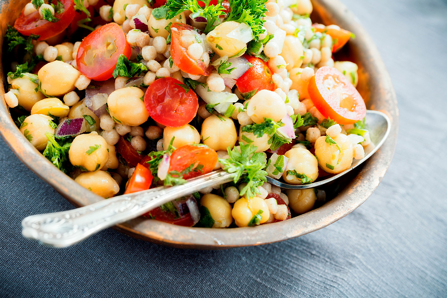 Ein Teller mit Couscous-Salat und Kirchererbsen steht auf einem gedeckten Tisch.