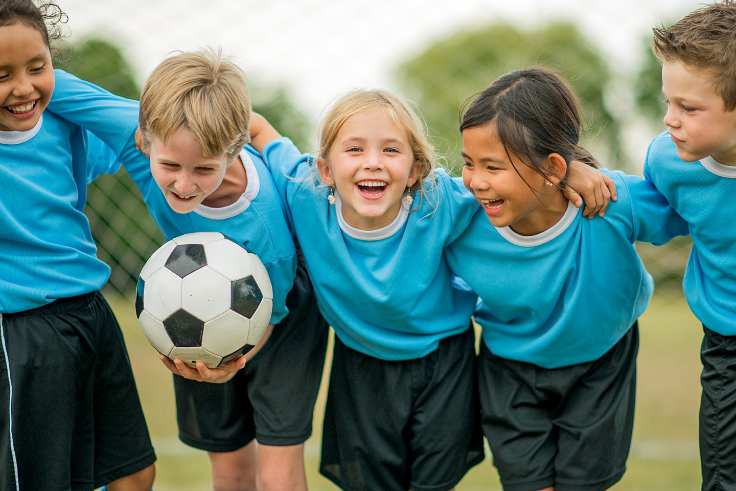 Fünf Fußball spielende Kinder umarmen sich und lachen.