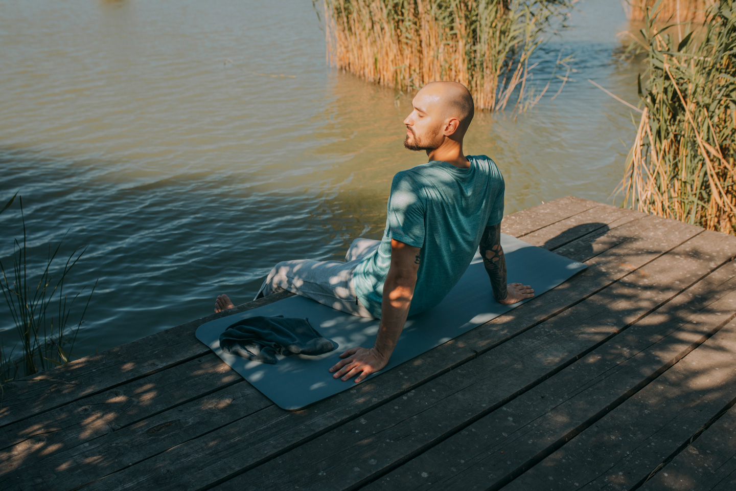 Ein Mann führt auf seiner Yogamatte am Wasser eine Achtsamkeitsübung zur Krebsbewältigung durch.