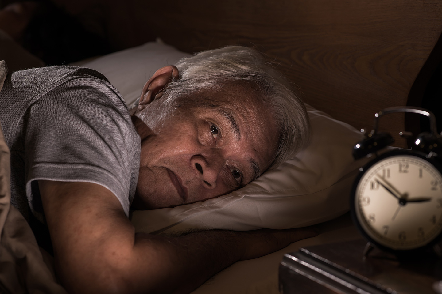 Älterer Mann liegt wach im Bett, weil er nicht schlafen kann.