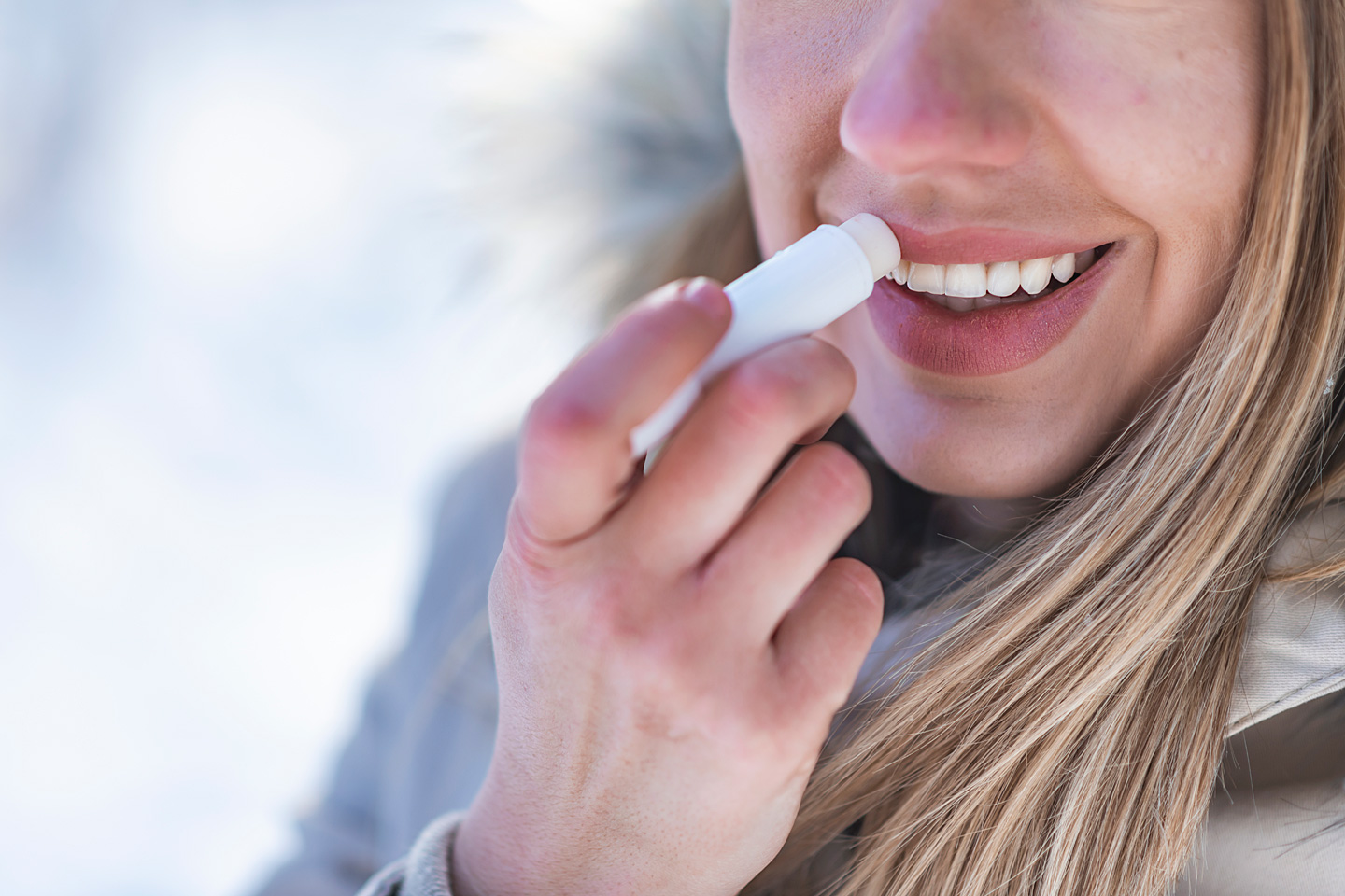 Eine Frau mit spröden Lippen pflegt ihre Lippen im Winter mit Lippenbalsam.