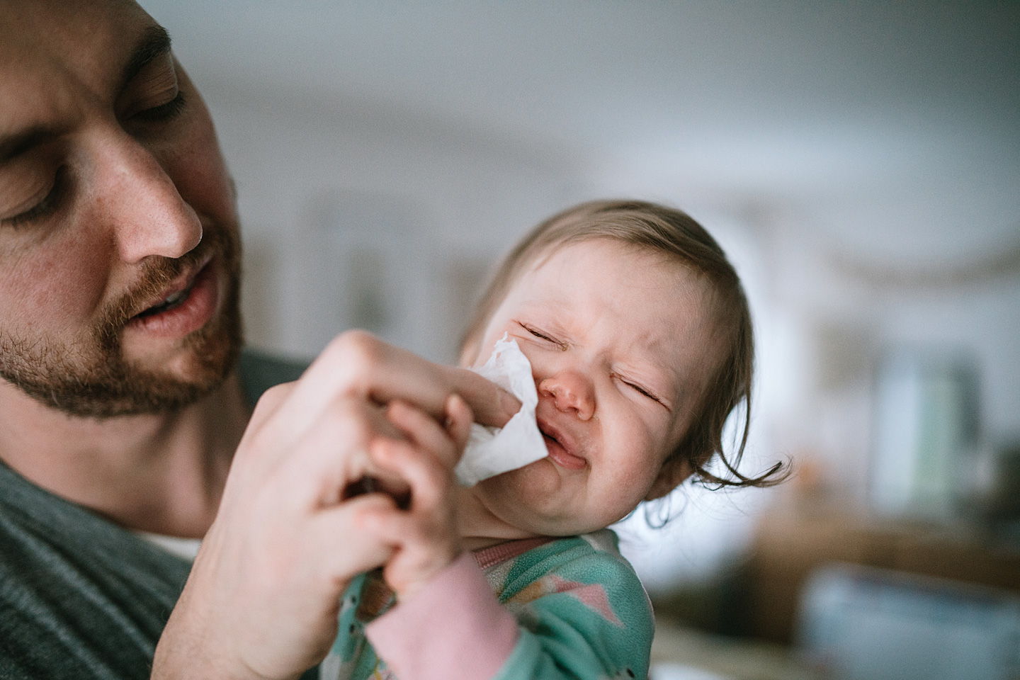 Ein Vater hält sein weinendes Kind mit Pseudokrupp auf dem Arm und wischt ihm mit einem Tuch den Mund ab.