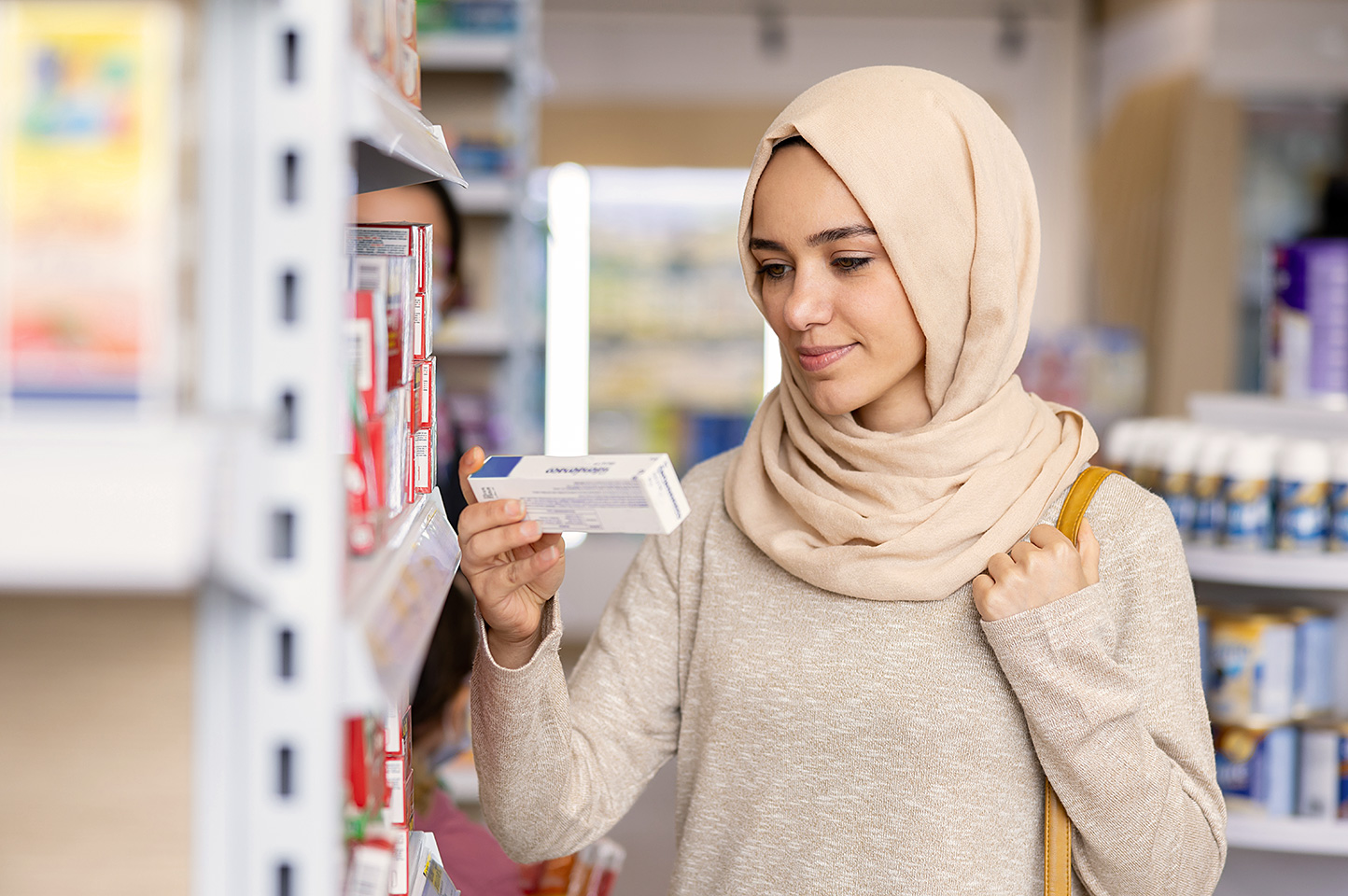 Eine junge Frau mit Hijab steht in einer Apotheke und liest die Aufschrift einer Medikamentenverpackung.