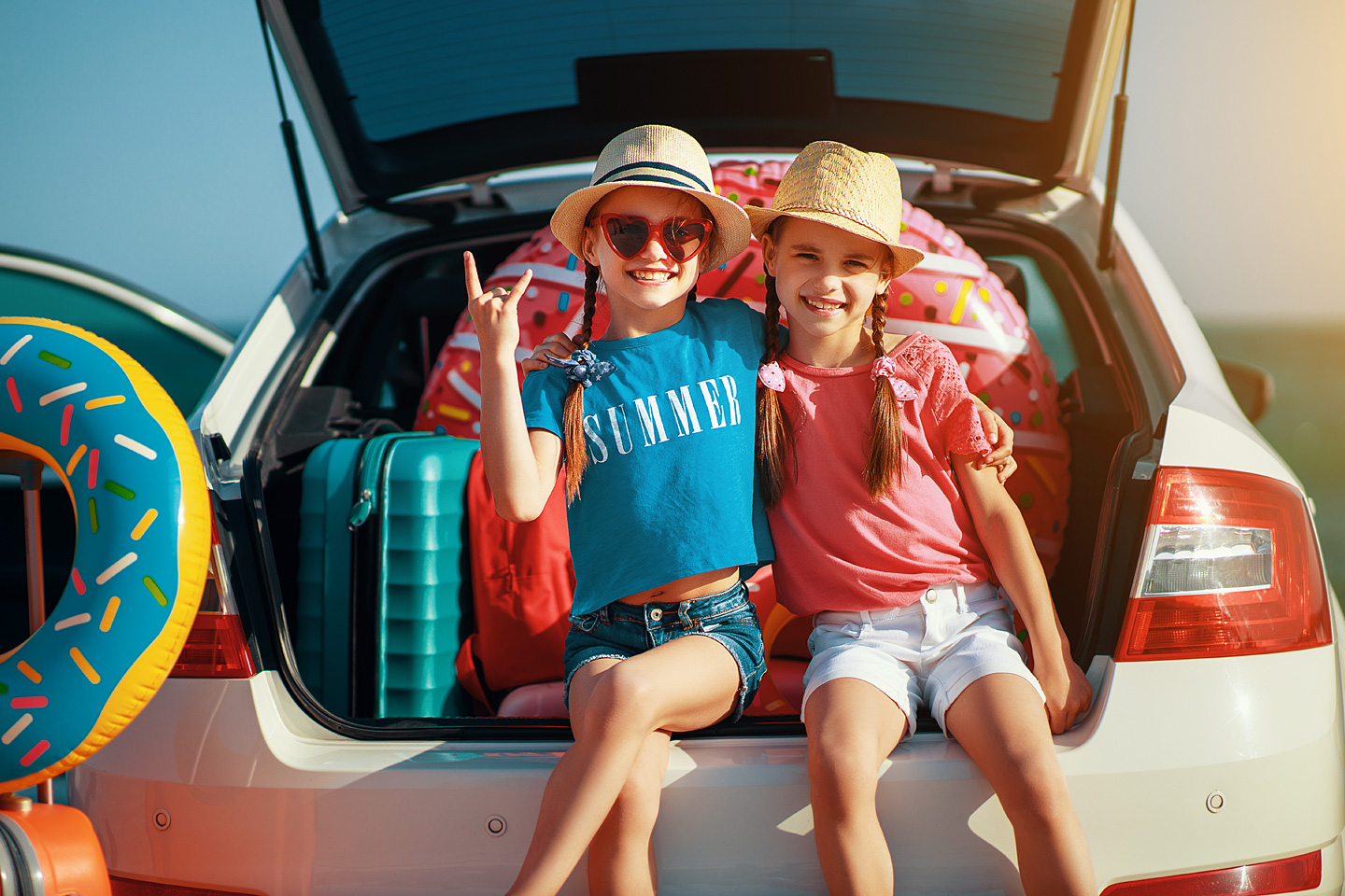 Kinder sitzen im Kofferraum mit Urlaubsgepäck und posieren