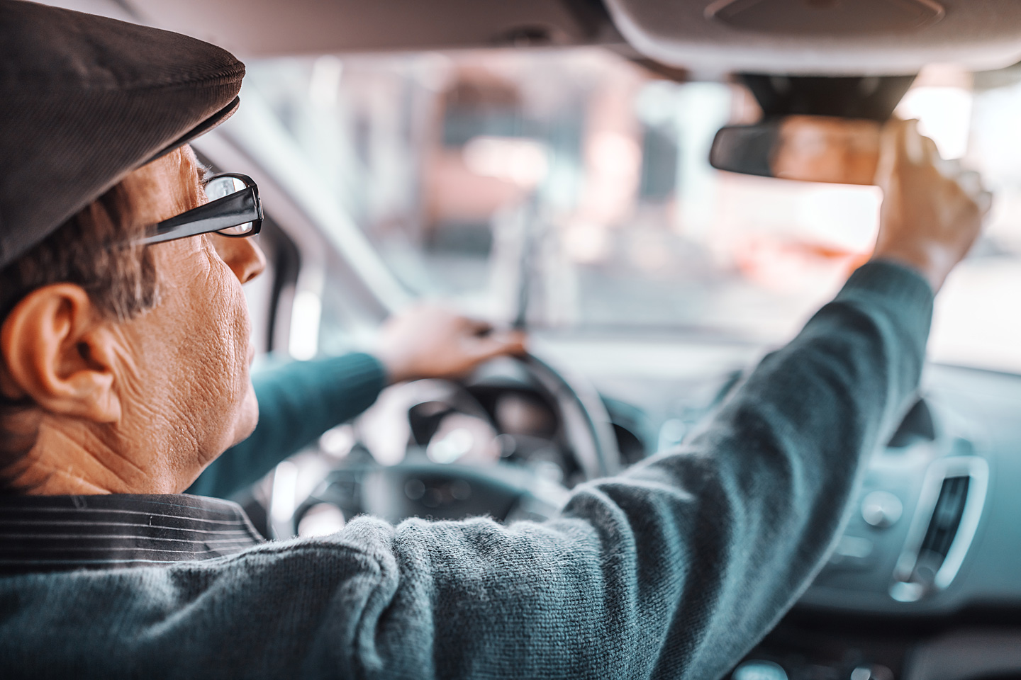 Ein älterer Autofahrer justiert den Rückspiegel seines Autos.