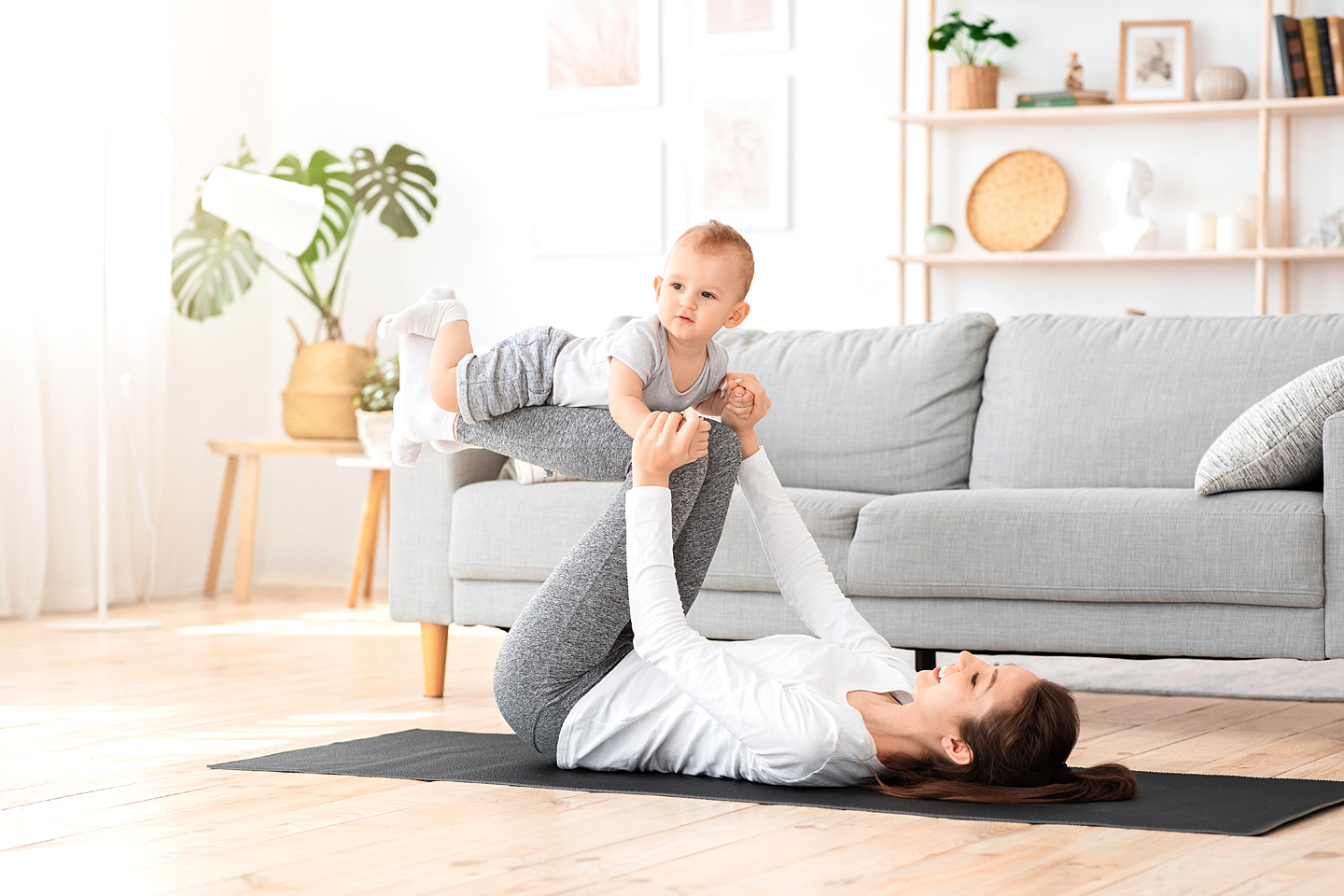 Eine junge Mutter macht Fitnessübungen und ihr Kind liegt auf ihren Beinen.