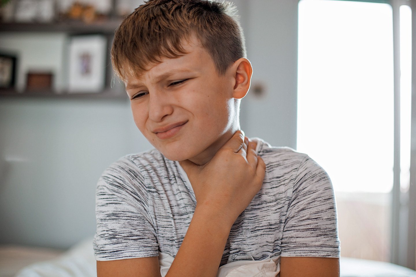 Ein Junge, der eine Mandelentzündung hat, fasst sich mit schmerzverzerrtem Gesicht an den Hals.