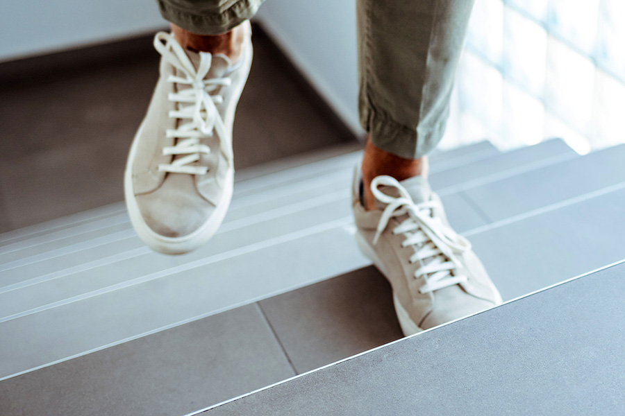 Im Bild sind zwei Füße in Sportschuhen zu sehen, die Treppen steigen.