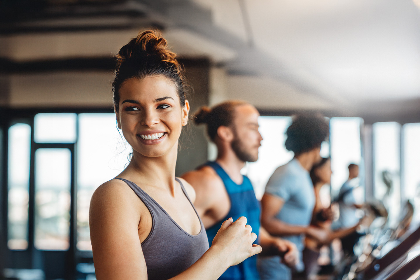 Eine junge Frau steht in einem Fitness-Studio auf einem Laufband und lacht in die Kamera
