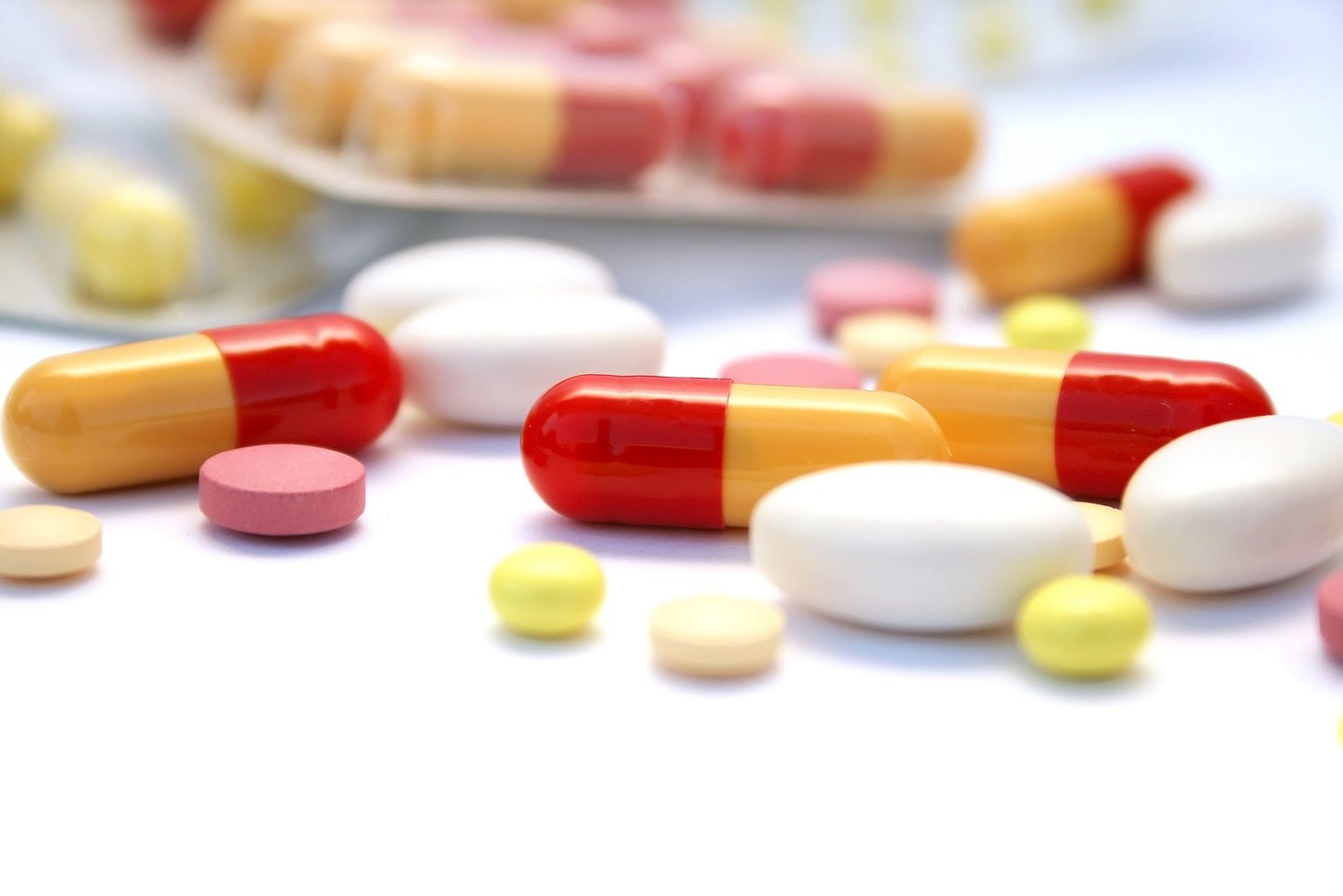 Foto von verschiedenen Pillen, Kapseln und Tabletten, die verteilt auf einer Oberfläche liegen.