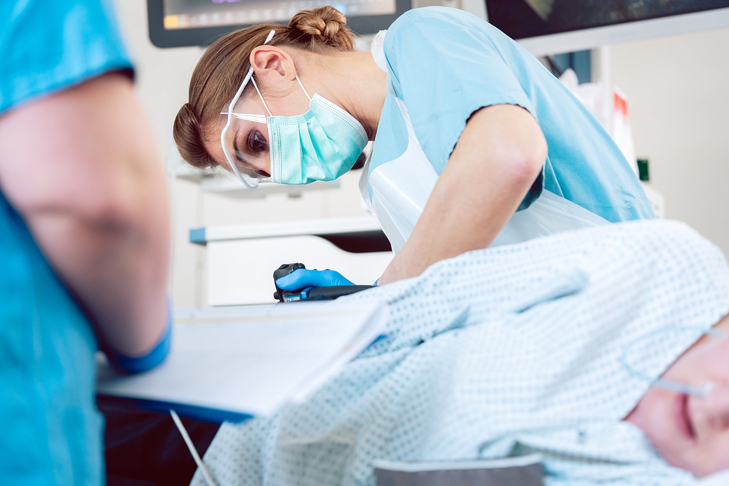 Foto zeigt eine narkotisierte Patientin bei der gerade eine Ärztin mit Mundschutz eine Koloskopie durchführt.