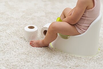 Ein kleines Kind sitzt auf seinem T&ouml;pfchen, Toilettenpapier liegt daneben.