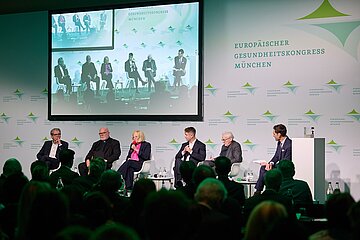Foto von der Diskussion mit Teilnehmerinnen und Teilnehmern beim Er&ouml;ffnungssymposium des Europ&auml;ischen Gesundheitskongress M&uuml;nchen 2026, darin von links nach rechts sichtbar: Andreas Storm (Vorstandsvorsitzender der DAK), Kardinal Reinhard Marx (Erzbischof von M&uuml;nchen und Freising), Dr. Irmgard Stippler (Vorstandsvorsitzende der AOK Bayern), Dr. Stefan Sch&ouml;ncke (Chefvolkswirt, Initiative Neue Soziale Marktwirtschaft), Prof. Dr. Dr. h. c. Karl Marx Einh&auml;upl (Kongresspr&auml;sident) und Prof. Dr. Andreas Belvers (Professor f&uuml;r Volkswirtschaftslehre und Gesundheits&ouml;konomie, Hochschulen Fresenius GmbH)
