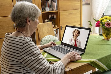 Telemedizin Eine ältere Dame ist bei einer Videosprechstunde zu Hause am Laptop.
