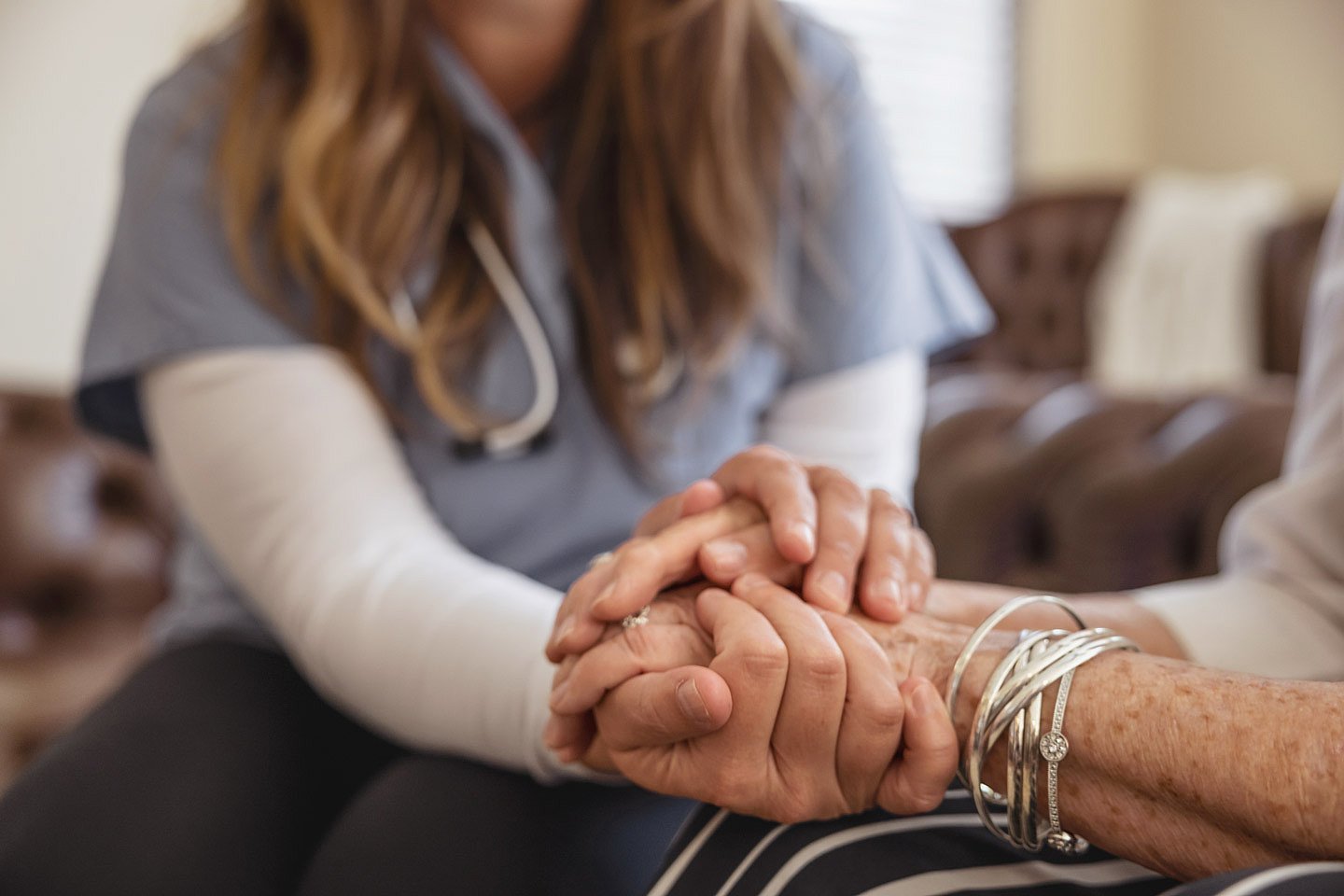 Pflege Foto: Eine Pflegerin umfasst die Hände einer Patientin mit ihren Händen.