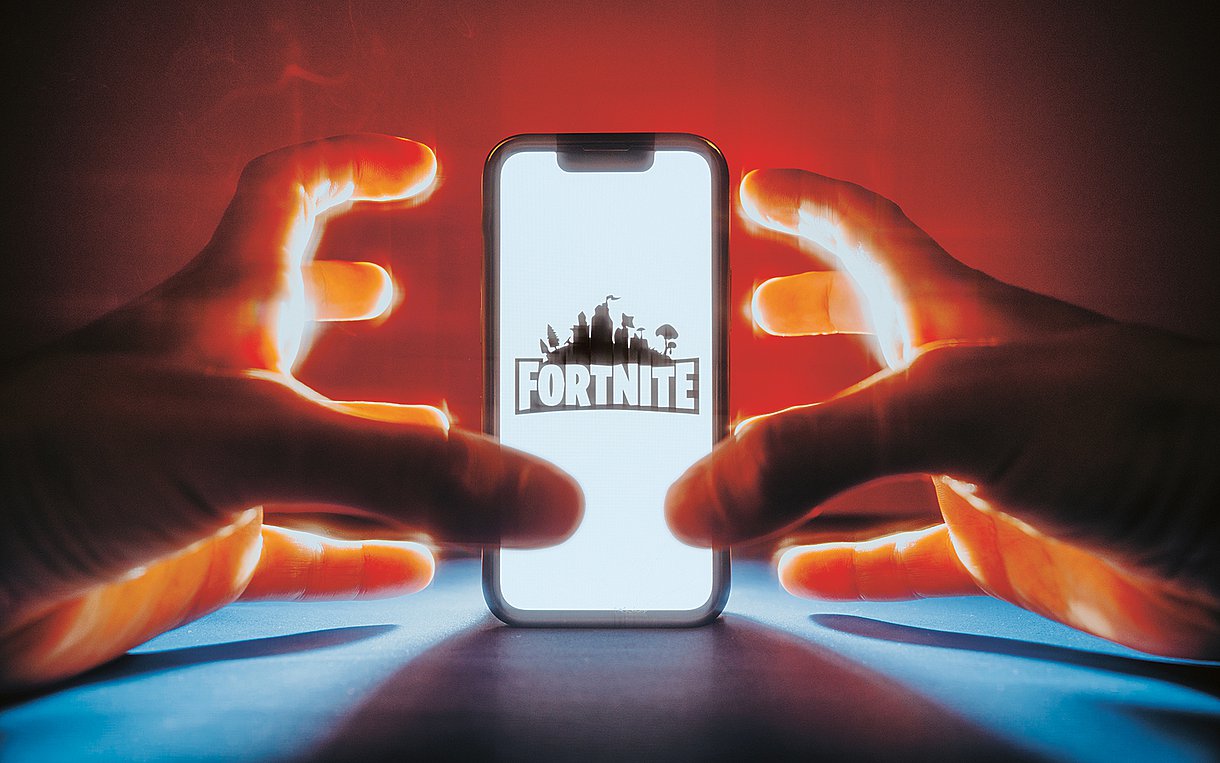 Foto eines Kindes, das am Smartphone Fortnite spielt. Es sind nur die Hände zu sehen.