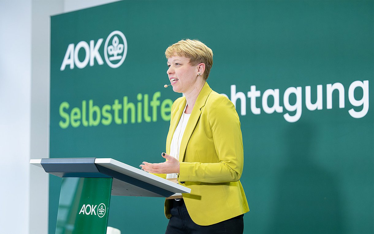 Saskia Weiß steht bei ihrem Vortrag auf der AOK-Selbsthilfe-Fachtagung am 12.1.2024 in Berlin hinter einem Rednerpult.