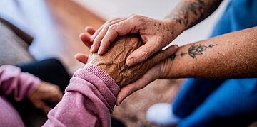 Eine Pflegende Person h&auml;lt die Hand einer alten Frau.
