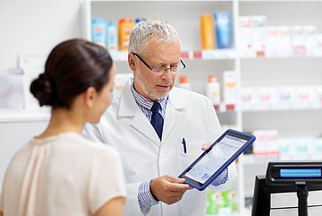 E-Rezept in Westfalen-Lippe Das Foto zeigt eine Frau in einer Apotheke, die sich ein Medikament abholt und mit dem Apotheker spricht.
