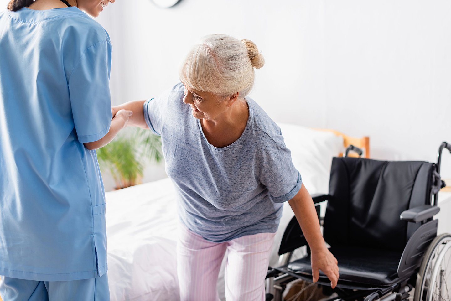 Eine Pflegekraft hilft einer älteren Patientin beim Aufstehen.