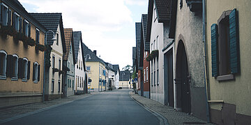 Eine Dorfstra&szlig;e, am Rand stehen aneinandergereihte H&auml;user.