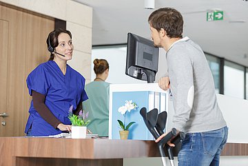 forsa-Ergebnisse zur Notfallversorgung in Schleswig-Holstein Ein Mann mit Krücken steht am Empfangstresen der Ambulanz eines Krankenhauses und spricht mit einer Angestellten.