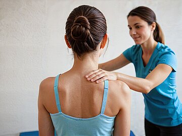 Eine Physiotherapeutin ber&uuml;hrt ihre Patientin an der Schulter.