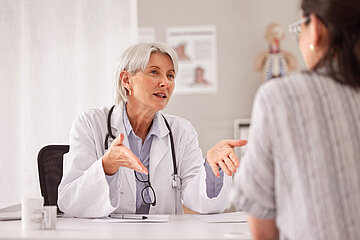 Foto: Eine &Auml;rztin spricht mit einer Patientin. Beide sitzen sich an einem Schreibtisch gegen&uuml;ber.
