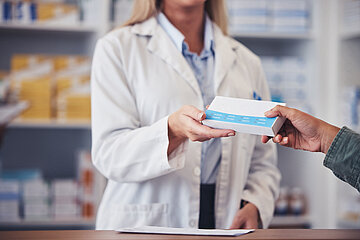 In einer Apotheke reicht eine Apothekerin einem Kunden eine Packung mit Medikamenten &uuml;ber den Tresen.
