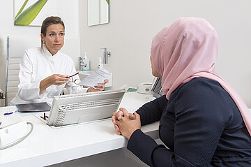 Eine Ärztin spricht mit einer Frau, die ein Kopftuch trägt.