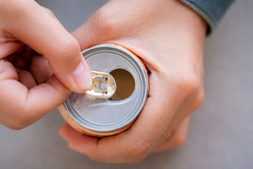 Ein paar jugendlicher H&auml;nde &ouml;ffnet eine Getr&auml;nkedose, die von oben zu sehen ist.