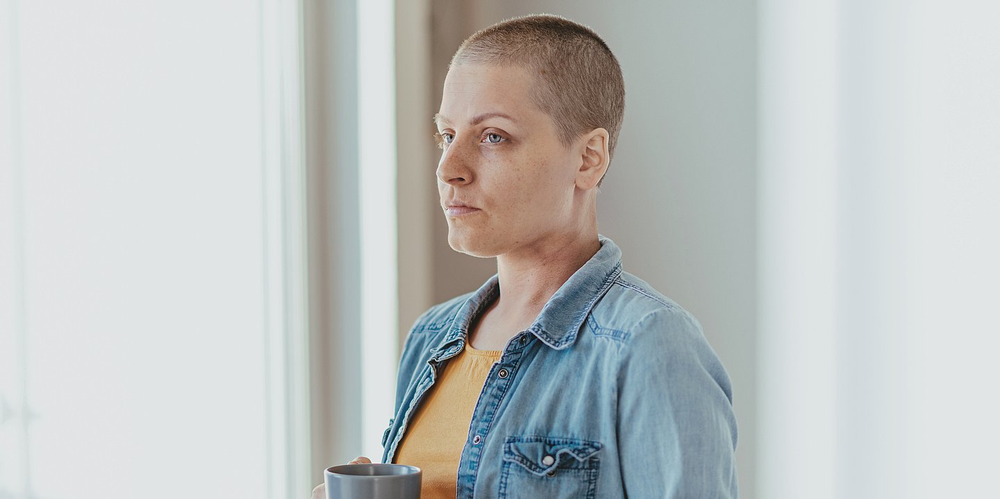 Foto: Eine Frau, die durch eine Chemotherapie sehr kurze Haare hat, schaut aus dem Fenster.
