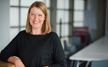 Das Portr&auml;t zeigt Daniela Sulmann. Sie hat blonde schulterlange Haare und tr&auml;gt einen dunklen Pullover. Sie l&auml;chelt in die Kamera.