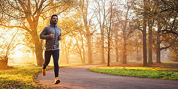 Foto: Ein Mann joggt im herbstlichen Park bei Sonnenaufgang.