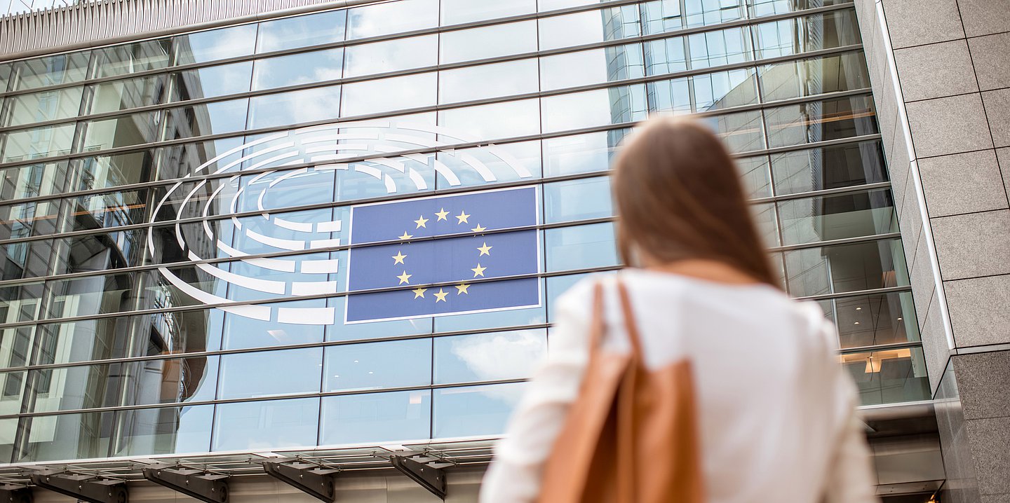 Foto einer Frau, die auf ein europäisches Regierungsgebäude mit der Europaflagge im Fenster blickt