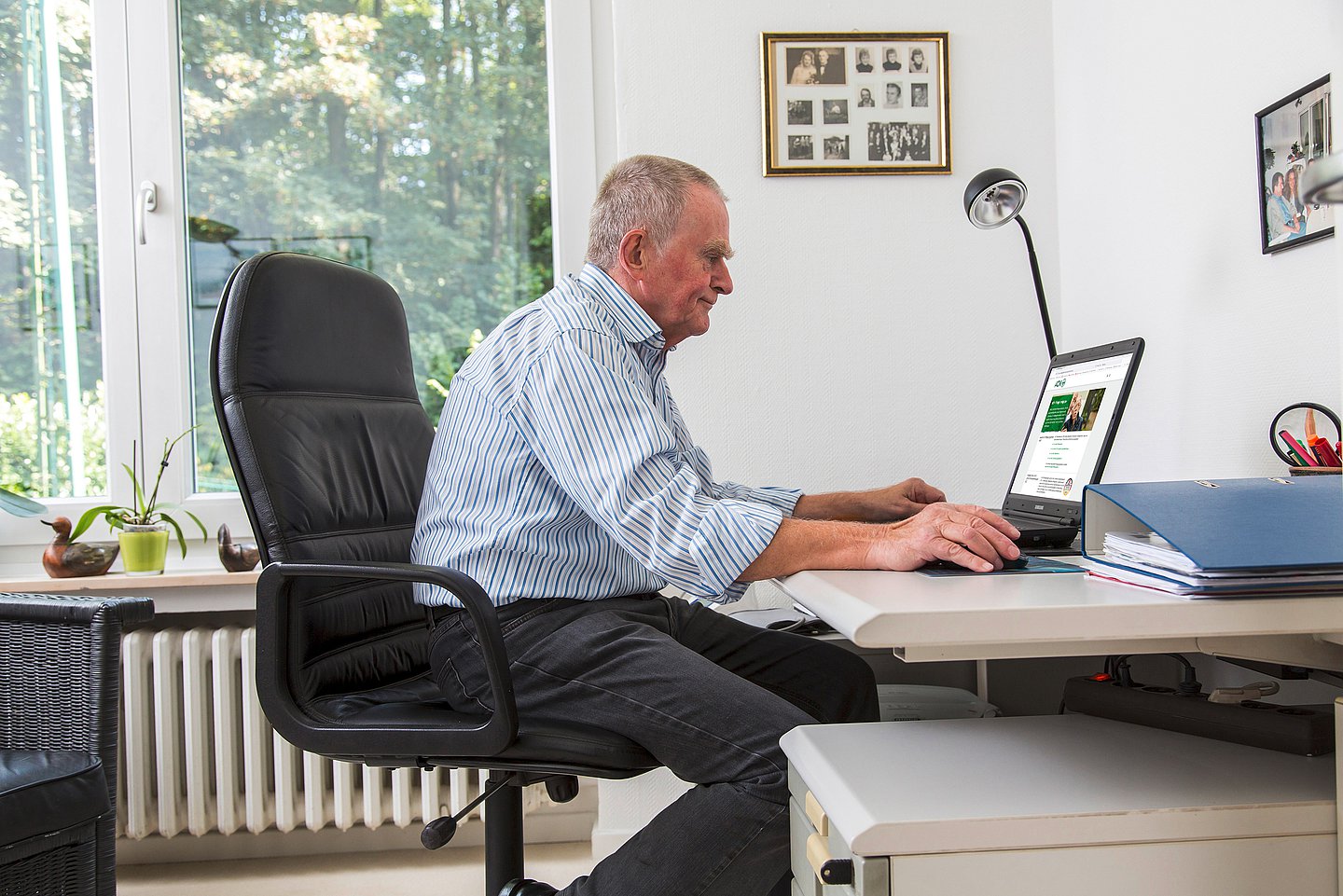 Foto: Ein älterer Mann sitzt am Schreibtisch und recherchiert an einem Laptop.