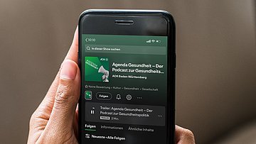 Podcast Zwei Hände halten ein Smartphone, auf dessen Display der Unternehmens-Podcast der AOK Baden-Württemberg zu sehen ist.