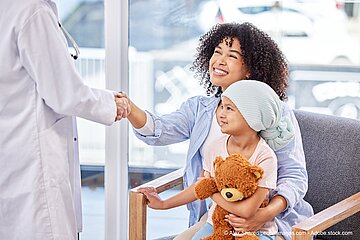Krebskrankes Kind sitzt auf dem Scho&szlig; seiner Mutter im Krankenhaus, die einer &Auml;rztin die Hand sch&uuml;ttelt