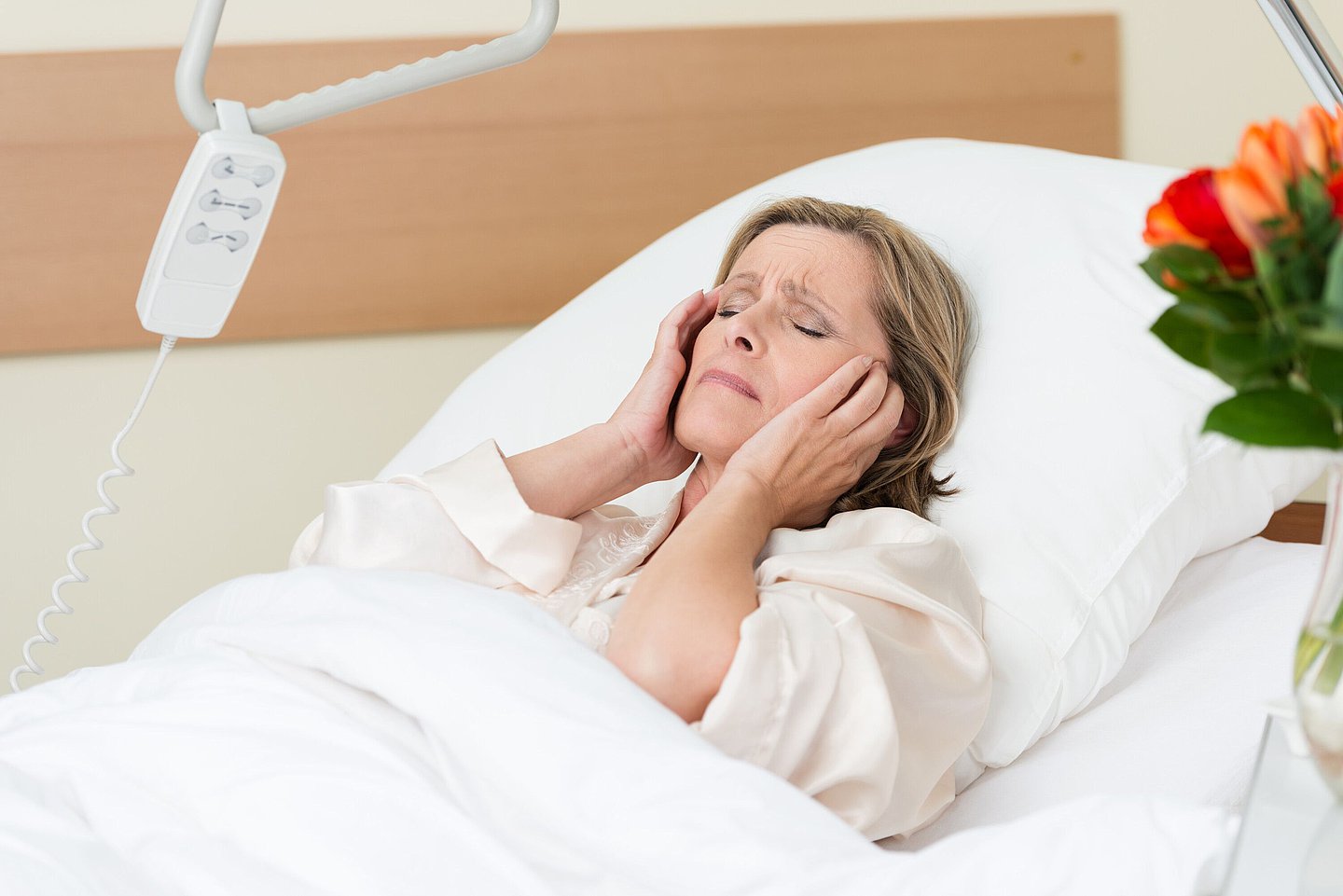 Eine Frau liegt mit Kopfschmerzen in einem Krankenhausbett.