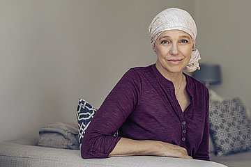 Frau mit Kopftuch Foto einer Frau auf dem Sofa sitzend, die sich an der Rückenlehne abstützt, mit einem Kopftuch, das sie offensichtlich nach einer Chemotherapie tragen muss