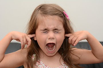 Kinder mit ADHS Ein kleines Mädchen hat die Zeigefinger in den Ohren und schreit.