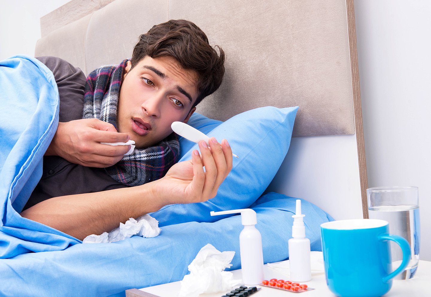 Foto zeigt einen kranken Mann, der mit Fieber im Bett liegt und einen grippalen Infekt auskuriert..