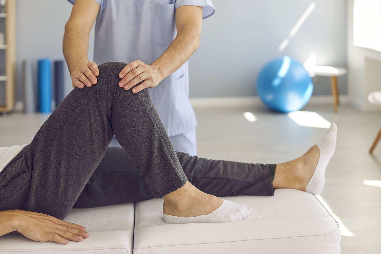 Das Foto zeigt einen Physiotherapeuten, der das Knie eines Patienten behandelt. 
