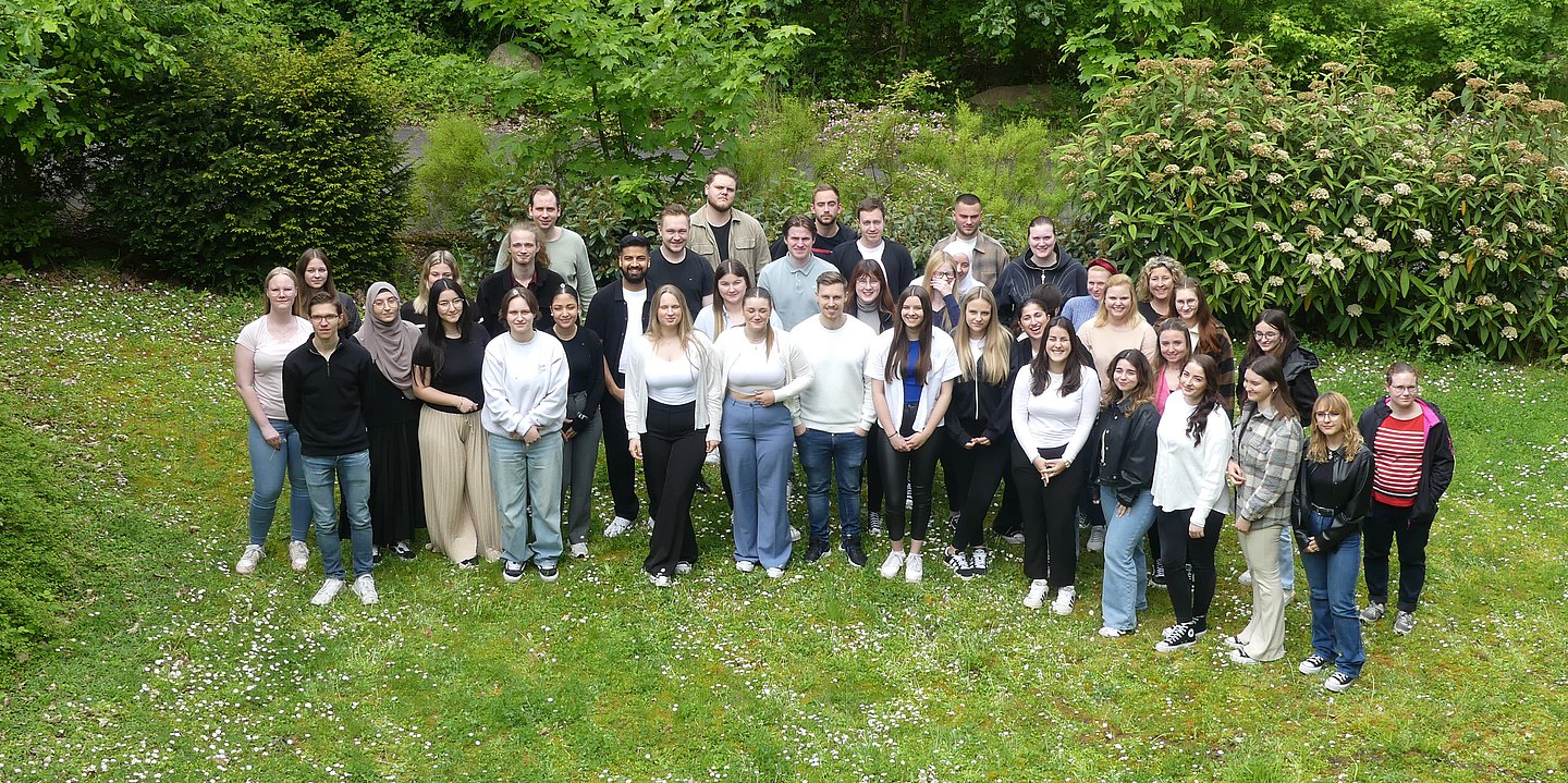 Das Foto zeigt die Gruppe aller Auszubildennen vor einem blühenden Gebüsch, die sich haben typisieren lassen. Aufnahme leicht von oben