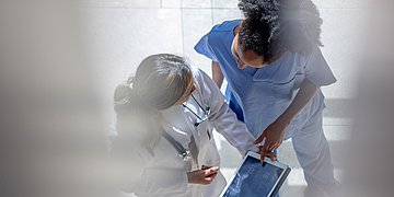 Eine Ärztin und eine Krankenschwester schauen gemeinsam auf ein Tablet. Man sieht sie von oben.