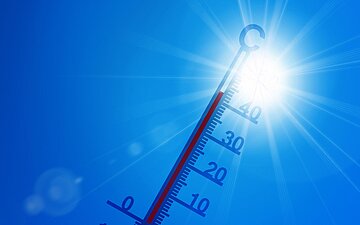 Symbolbild f&uuml;r Hitze: Ein Thermometer vor der Sonne am wolkenlosen Himmel